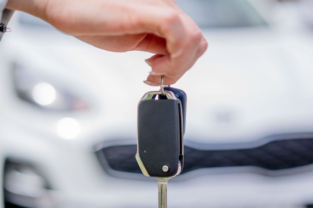 A hand holding a vehicle key in front of a car